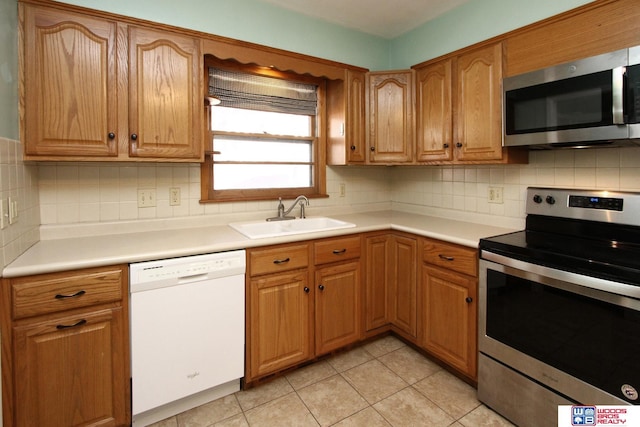 kitchen featuring light tile patterned flooring, stainless steel appliances, a sink, light countertops, and decorative backsplash