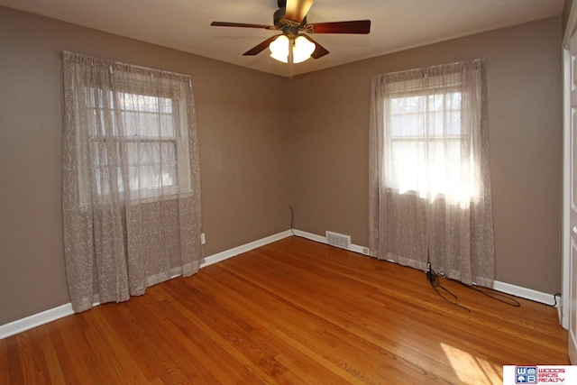 empty room featuring ceiling fan, wood finished floors, visible vents, and baseboards