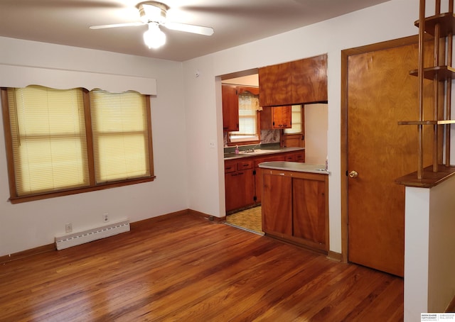 kitchen with a baseboard radiator, a ceiling fan, brown cabinetry, wood finished floors, and baseboards