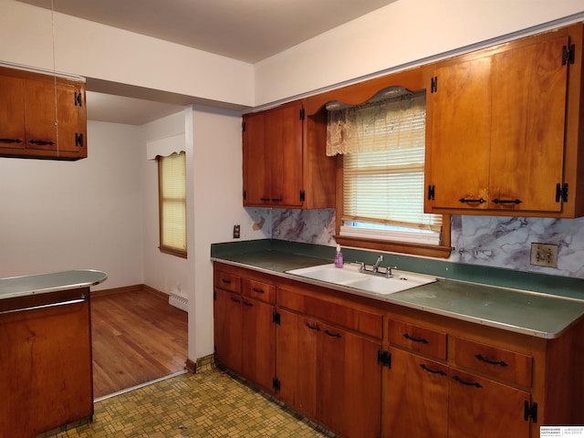 kitchen with brown cabinetry, a sink, baseboards, and tasteful backsplash