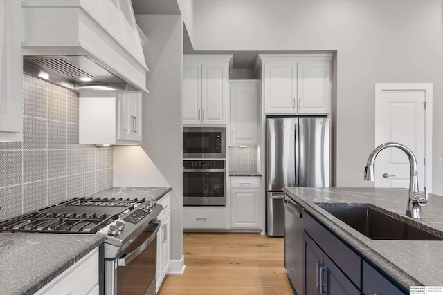 kitchen featuring premium range hood, a sink, white cabinetry, appliances with stainless steel finishes, and light wood-type flooring