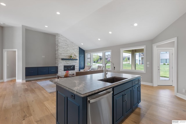 kitchen with lofted ceiling, stainless steel dishwasher, a kitchen island with sink, a sink, and a stone fireplace