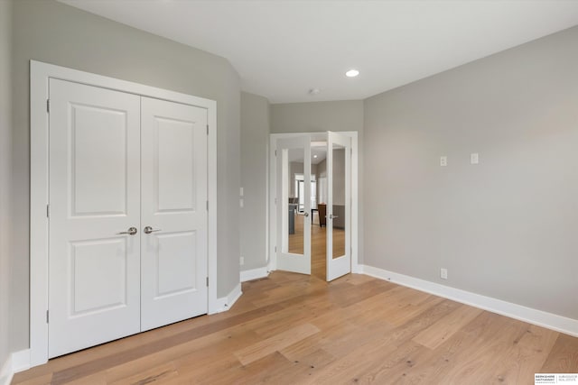 unfurnished bedroom featuring baseboards, french doors, light wood-style floors, a closet, and recessed lighting