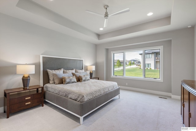 bedroom with visible vents, a tray ceiling, baseboards, and light colored carpet