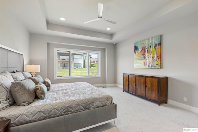 bedroom featuring light carpet, a raised ceiling, and baseboards