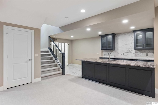 kitchen featuring recessed lighting, light colored carpet, backsplash, glass insert cabinets, and light stone countertops