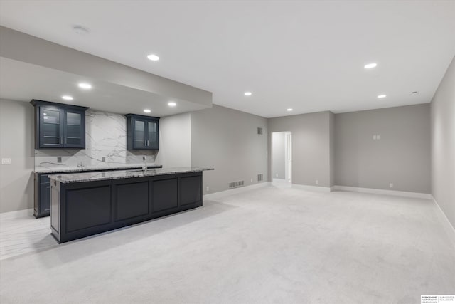 kitchen featuring light carpet, recessed lighting, a kitchen island with sink, and decorative backsplash