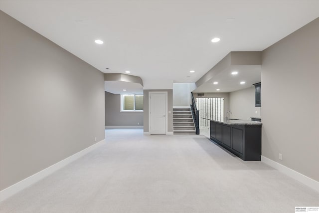 unfurnished living room with stairway, a sink, light colored carpet, and baseboards