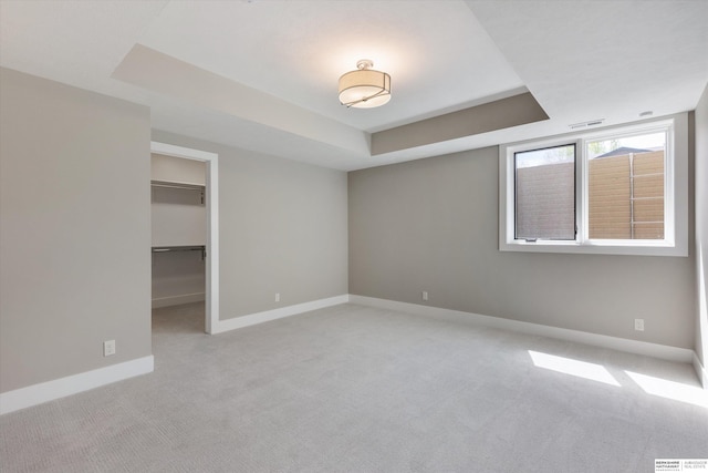 unfurnished bedroom with carpet flooring, visible vents, baseboards, a walk in closet, and a raised ceiling