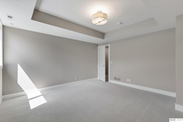 empty room with carpet floors, a raised ceiling, visible vents, and baseboards