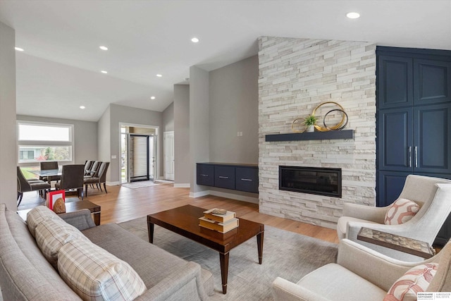 living area with baseboards, lofted ceiling, light wood-style flooring, a fireplace, and recessed lighting