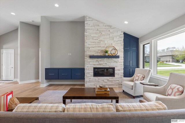 living area with light wood-type flooring, recessed lighting, vaulted ceiling, and a stone fireplace