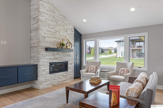 living area with light wood finished floors, baseboards, a stone fireplace, high vaulted ceiling, and recessed lighting