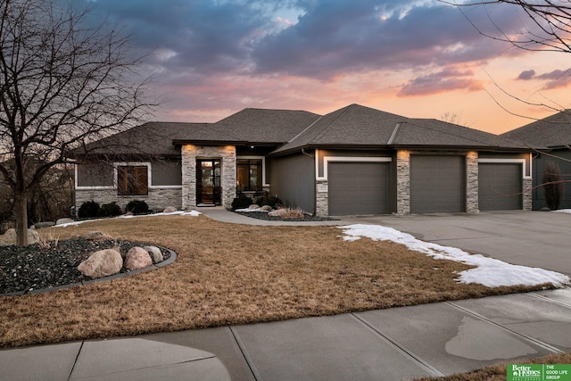 prairie-style home featuring an attached garage, a shingled roof, stone siding, driveway, and a front yard