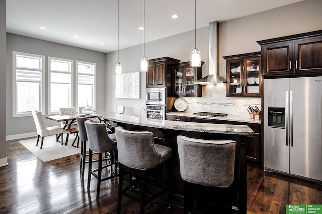 kitchen with wall chimney exhaust hood, appliances with stainless steel finishes, dark brown cabinetry, and tasteful backsplash