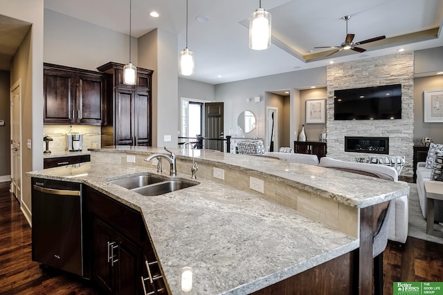 kitchen with dark brown cabinetry, dishwasher, dark wood-style flooring, a fireplace, and a sink