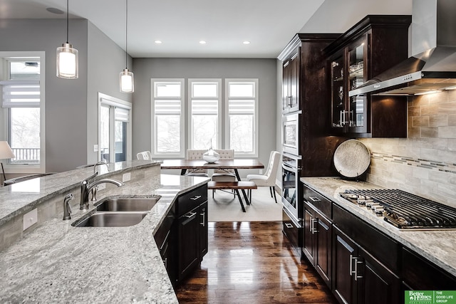 kitchen featuring dark wood-style floors, appliances with stainless steel finishes, light stone countertops, wall chimney range hood, and a sink