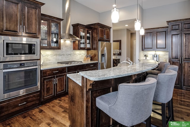 kitchen with stainless steel appliances, a breakfast bar, wall chimney exhaust hood, and dark wood-style flooring