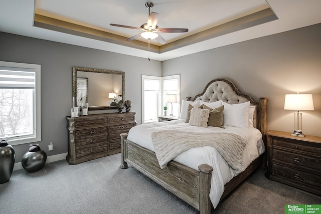 carpeted bedroom featuring baseboards, a raised ceiling, and a ceiling fan