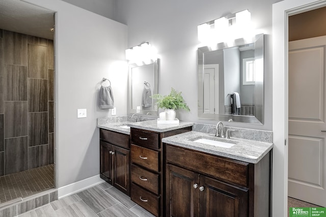 full bath featuring baseboards, tiled shower, and vanity