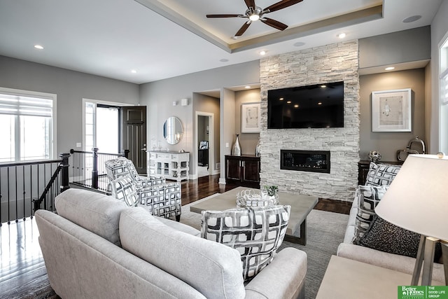 living room with dark wood-type flooring, a tray ceiling, a fireplace, and ceiling fan