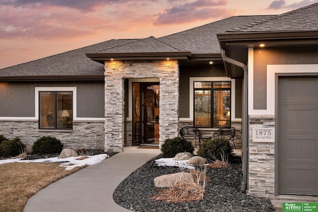 property entrance with an attached garage, stone siding, a shingled roof, and stucco siding