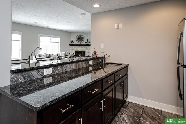 kitchen featuring a textured ceiling, baseboards, a sink, and a stone fireplace