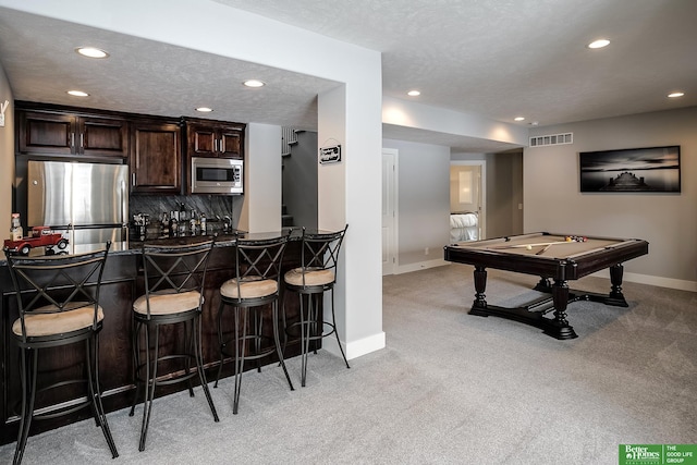 interior space featuring stainless steel appliances, dark countertops, visible vents, dark brown cabinets, and a kitchen bar