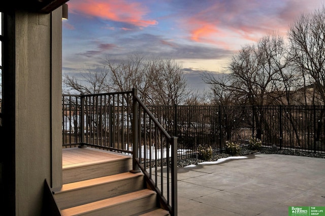 patio terrace at dusk featuring fence and a wooden deck