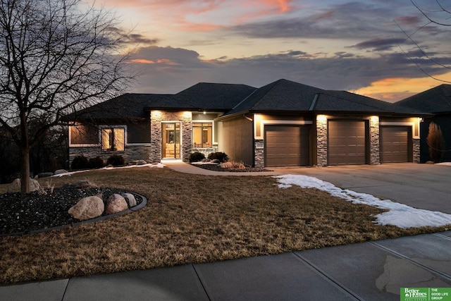 prairie-style home featuring a garage, stone siding, driveway, and stucco siding