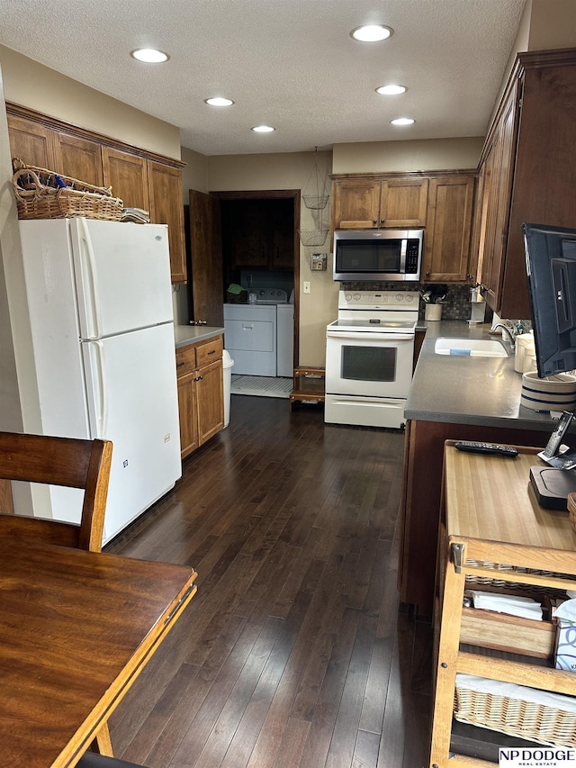 kitchen with dark wood-style floors, a sink, a textured ceiling, separate washer and dryer, and white appliances