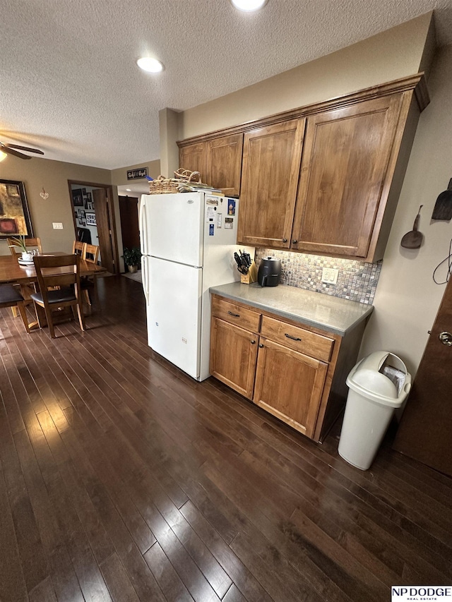 kitchen with dark wood-type flooring, freestanding refrigerator, brown cabinetry, and tasteful backsplash