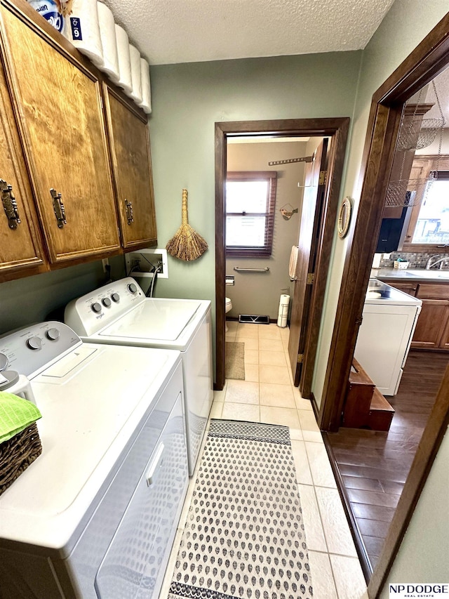 washroom featuring cabinet space, light tile patterned flooring, a textured ceiling, and independent washer and dryer