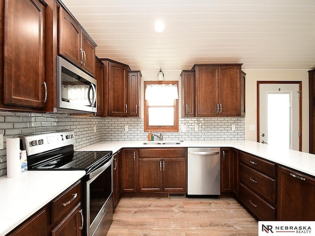 kitchen featuring a sink, stainless steel appliances, light countertops, light wood-type flooring, and backsplash