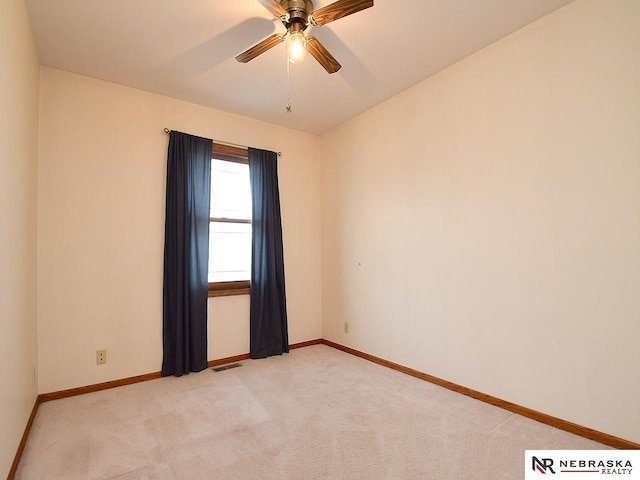 spare room with a ceiling fan, light colored carpet, visible vents, and baseboards