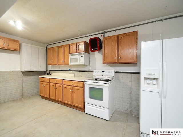 kitchen with white appliances, brown cabinetry, brick wall, unfinished concrete floors, and light countertops