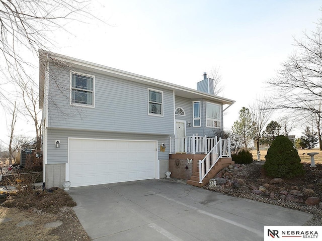 raised ranch with an attached garage, driveway, and a chimney