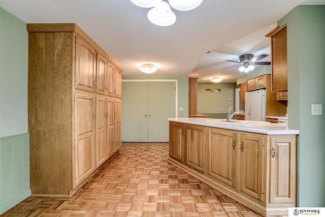 kitchen with ceiling fan, freestanding refrigerator, a peninsula, light countertops, and a sink