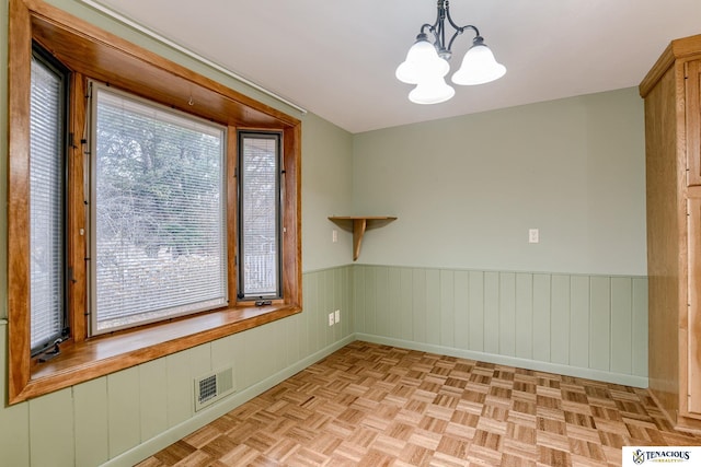 spare room featuring a healthy amount of sunlight, visible vents, and a wainscoted wall