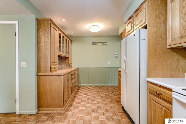 kitchen featuring recessed lighting, a wainscoted wall, light countertops, freestanding refrigerator, and glass insert cabinets