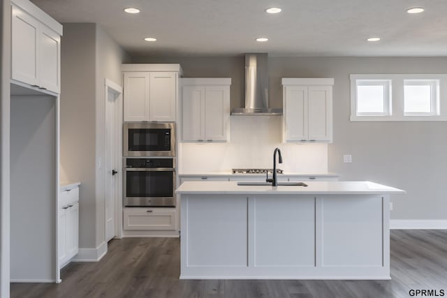 kitchen with appliances with stainless steel finishes, light countertops, a sink, and wall chimney range hood