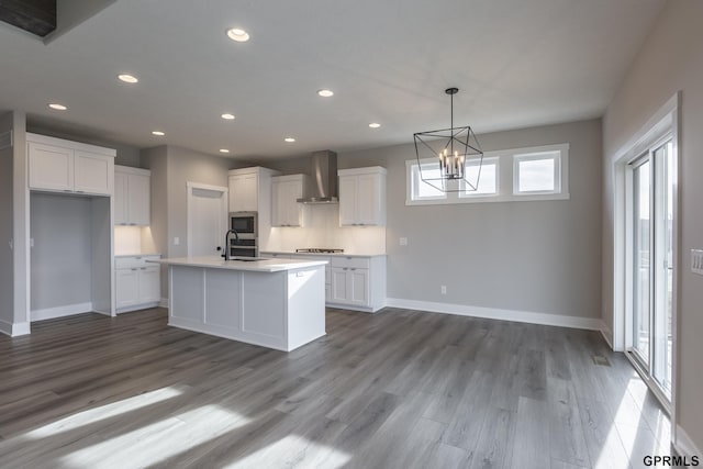 kitchen with white cabinets, an island with sink, stainless steel microwave, wood finished floors, and wall chimney range hood