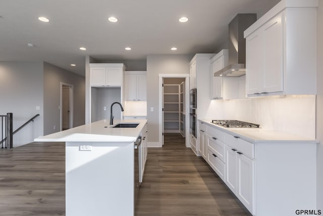 kitchen with stainless steel appliances, tasteful backsplash, white cabinets, a sink, and wall chimney exhaust hood