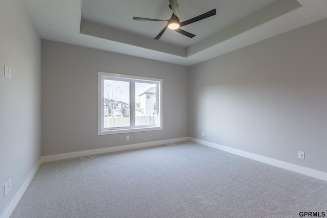 empty room featuring a tray ceiling, carpet flooring, and baseboards