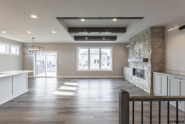 unfurnished living room featuring baseboards, wood finished floors, an inviting chandelier, a fireplace, and recessed lighting