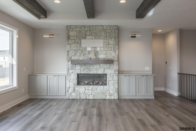 unfurnished living room featuring beamed ceiling, a fireplace, wood finished floors, and baseboards