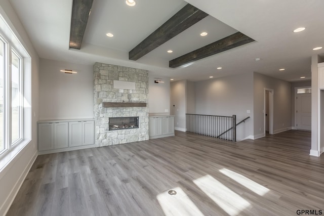 unfurnished living room featuring recessed lighting, beam ceiling, a fireplace, and wood finished floors