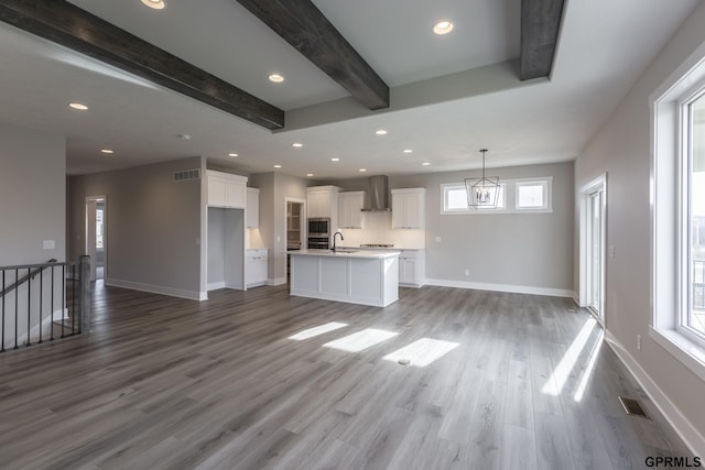 unfurnished living room featuring beam ceiling, baseboards, a sink, and wood finished floors