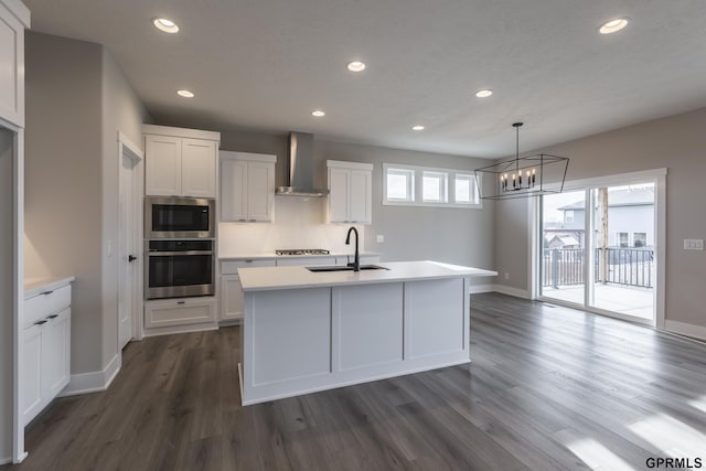 kitchen with white cabinets, appliances with stainless steel finishes, wall chimney range hood, a sink, and recessed lighting