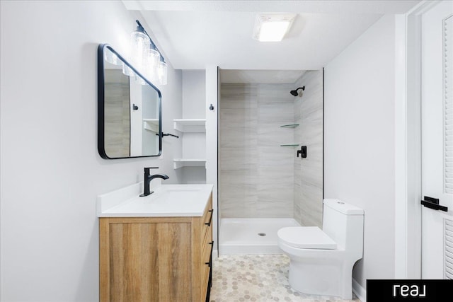 bathroom with toilet, tiled shower, and vanity